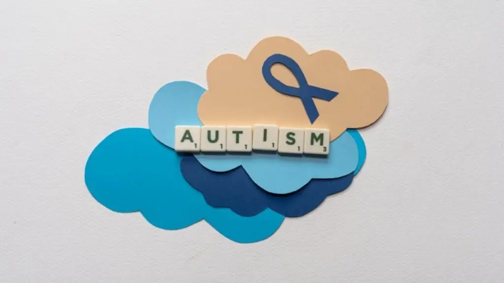 Quotes autism awareness concept with the word “autism” displayed on paper cloud cutouts, accompanied by a blue ribbon symbolizing support and hope.