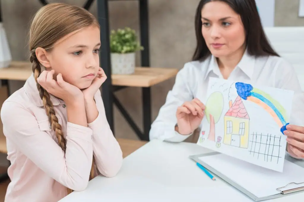 young female psychologist showing drawing paper with drawn house sad serious girl 1